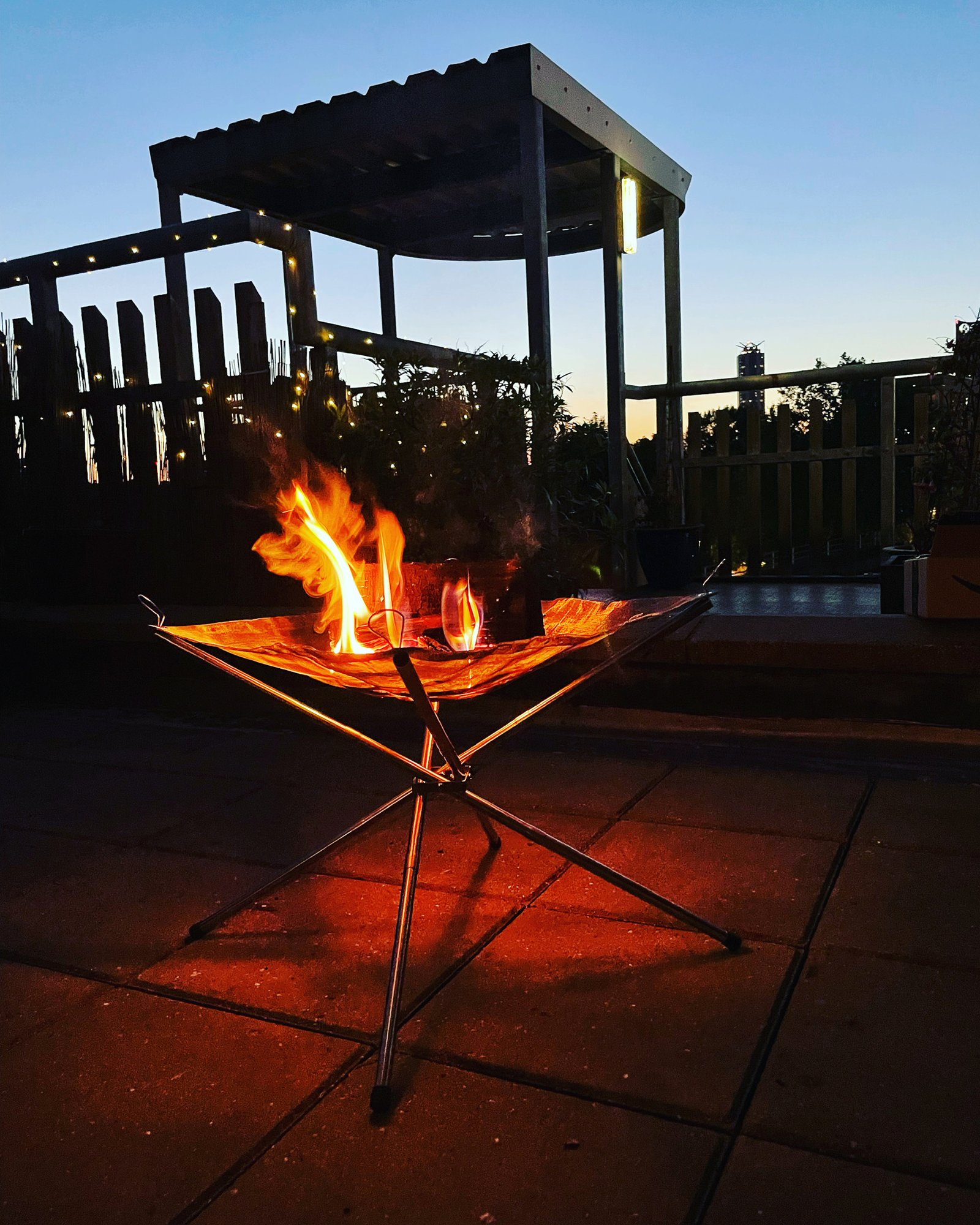 Fire pit on the terrace at dusk, festoon lights and pergola behind