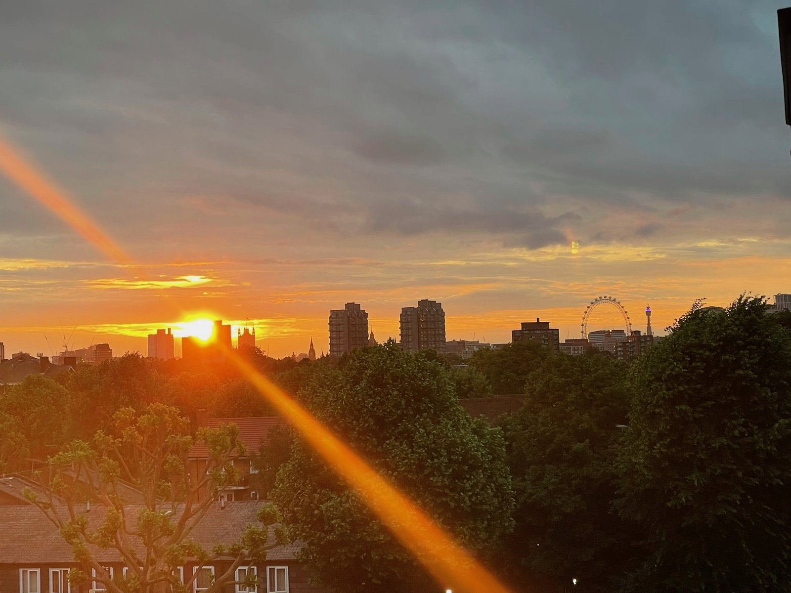 Sun bursting through cloud over the London Eye and BT Tower, summer evening